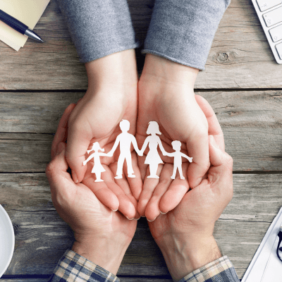 Um casal segurando nas mãos recortes em papel que representam uma família